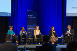 Photo of five people seated on a stage with the MITEI logo in the background