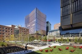 Photo of MIT buildings centered on 314 Main Street, a 17-story glass building. A courtyard with grass, tables, chairs, and walkways is in the foreground.
