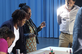 Photo of four people standing over a table with Lego-like models on it