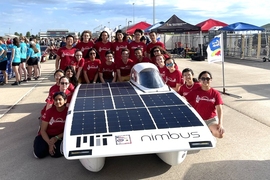 A team of 20 students crowds around the Nimbus solar car, wearing their red S.E.V.T. shirts