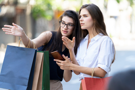 Photo of two women on the street intently gazing and pointing at something off-camera. One is giving directions to the other.