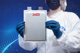 A person wearing a cleanroom suit holds a 24M rectangular silver bag, like a mailing sleeve, that holds the thin battery cell inside.