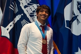 Vishnu Jayaprakash stands with a gold medal around his neck in front of two flags