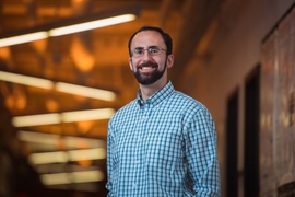 Koroush Shirvan in an interior hallway with lights overhead in a zig-zag pattern casting an orange light