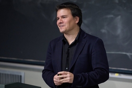 Pablo Jarillo-Herrero, wearing a dark jacket and holding his hands together speaks in front of a blackboard