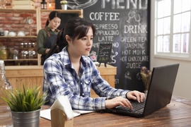 Photo of a young woman working on her laptop at a table in a cafe