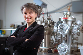  MIT Professor Bilge Yildiz stands with arms folded in her MIT lab with large metallic equipment behind her