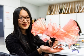 In a small studio, Shua Cho holds up a pink glass flower-like object