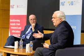 Frederick Smith and Yossi Sheffi sit around a small coffee table in discussion with MIT banners behind them