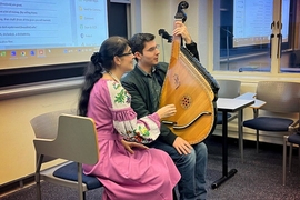 A woman in traditional Ukrainian dress instructing a student holding a large stringed instrument