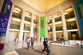 MIT's Lobby 7, which features three levels of walkways supported by columns and large banners with a few people walking t hrough