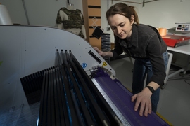 Erin Doran stands over a textile weaving machine demonstrating how a fabric is woven on it.