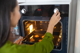 Photo in which the viewer looks over the shoulder of a young woman as she adjusts a dial on her oven, setting it to 350 degrees