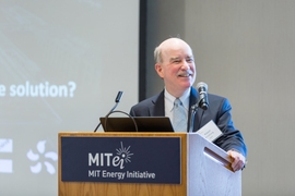 Robert Armstrong grips a lecturn with the MITEI logo, with projector screen behind him.