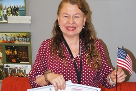 Photo of Sally Romero holding an American flag in one hand and two certificates in the other.