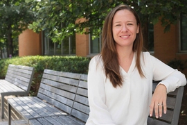 Sara Prescott sitting on an outdoor bench in front of some trees on a sunny day