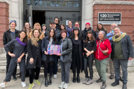 20 people pose for a group photo in front of large doors and sign reading "MIT Building W31"