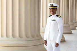 Crystan McLymore dressed in white U.S. Navy uniform stands outside by building columns on MIT campus