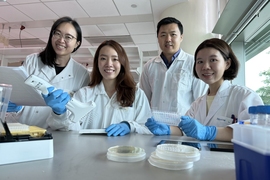 Four researchers in white lab coats and blue nitrile gloves pose at a bench