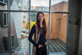 Cathy Wu standing in front of a window. Behind her are various oddly-angled facets of the MIT Stata Center in a mix of materials — metal, brick, glass — and colors — silver, tan, bright yellow.