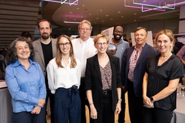 Eight smiling people pose for a group photo at an indoor cocktail reception.