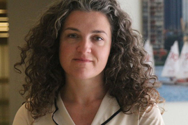 Lerna Ekmekciouglu in front of a window with sailboats on the Charles River in the background. 