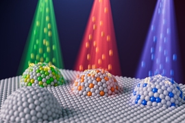 Artist’s concept of four domes comprised of spheres representing nanoparticles. Three of the domes have different colored particle beams shining down on them. 