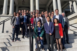 About 30 people, including 26 MIT students, pose on the steps of the Eisenhower Executive Office Building.