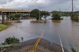 Photo of a flooded street with a bridge in the background on a cloudy day