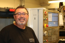 Pat McAtamney smiles in front of a large machine inside a cement brick room