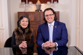 Lisa Yang and Amos Winter pose for a photo. They sit together at a black table in a white room with an intricately carved wooden dresser and a Buddah head statue in the background.