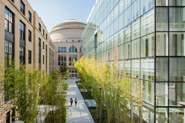 Exterior photo of the all-glass MIT.nano, at right; the brick Main Group building, at left; and a courtyard pathway down the middle, with MIT Dome in the background
