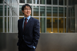 William Li stands outside and looks to the right. Rows of windows are in the background.