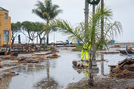 A worker cleans up a flooded, debris-filled street after a bomb cyclone hit Santa Cruz, CA.