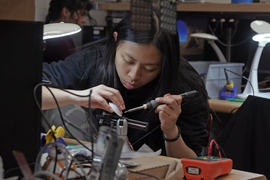 Seated at a lab table, Audrey Chen solders a circuit board