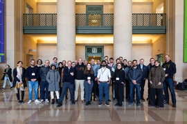 A group of 30 people stand in Lobby 7 at MIT, a large atrium with multiple floors