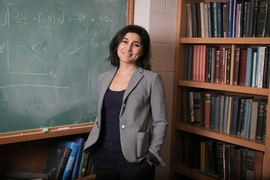 Lydia Bourouiba stands near a full bookshelf and chalk board.