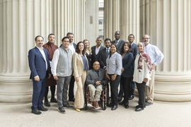 16 people pose between rows of large columns