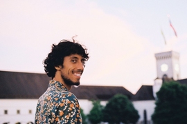 Bernardo Picão smiles at the camera looking over his shoulder. An out-of-focus clock tower is seen the background.