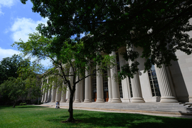 People walk under the trees and columns of Killian court.