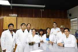 Nine people around a table in a lab, wearing lab coats and smiling