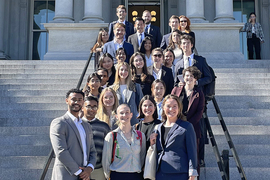 25 people pose on the stairs outside a colonaded portico