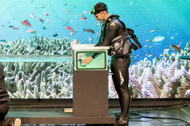 A scuba diver puts goggles in an aquarium while on stage