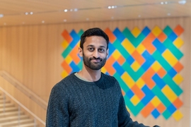 Manish Raghavan stands before a colorful geometric wall-hanging