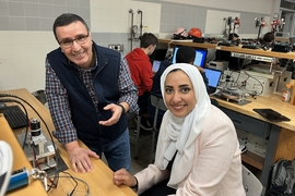 Kamal Youcef-Toumi and Amira Alazmi pose in a bench lab filled with technical equipment