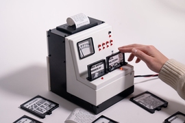 A hand interacts with a box-like game interface, inserting a cartridge while a paper scroll prints out news alerts. One inserted cartridge says "Check Whatsapp messages of" and another says "Local politicians."