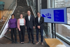 Four people pose in front of a staircase and a screen that says "SLB"