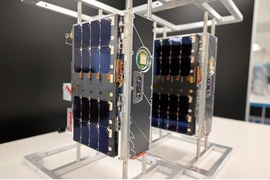 On a tabletop, two small boxy satellites, roughly 20 x 10 x 30 cm in size.
