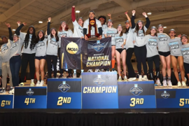 Several MIT students stand atop a six-tier NCAA championship podium inside a field house; Alexis Boykin of MIT holds the national trophy.