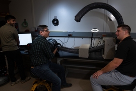 Ankush Dhawan, Chad Council, and Nathaniel Hanson in a dark lab test a vine robot, a 10-foot long bendy tube